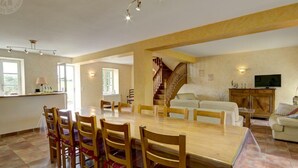 Een ruime woonkamer met een grote houten eettafel, omringd door stoelen, een trap naar een verdieping en een televisie op een houten kast.