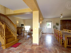 A spacious living area with a wooden staircase, a dining table with chairs, and a kitchen area. - Spacious house with heated pool, 4 bedrooms in Chalain-le-Comtal (Chalain-le-Comtal)