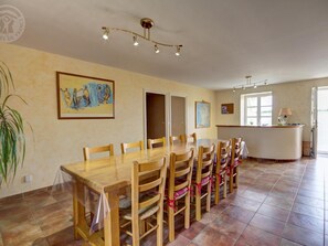 Un espace repas avec une table et des chaises en bois, un comptoir d’accueil et un tableau accroché au mur.