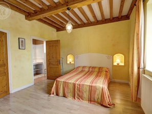 Un dormitorio con una cama, vigas de madera en el techo, un armario y dos lámparas de pared.