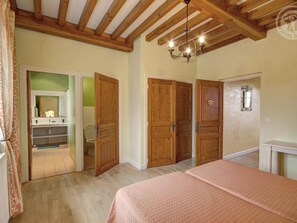 Une chambre avec des portes en bois, un lit recouvert d’une couvre-lit rose et un lustre.