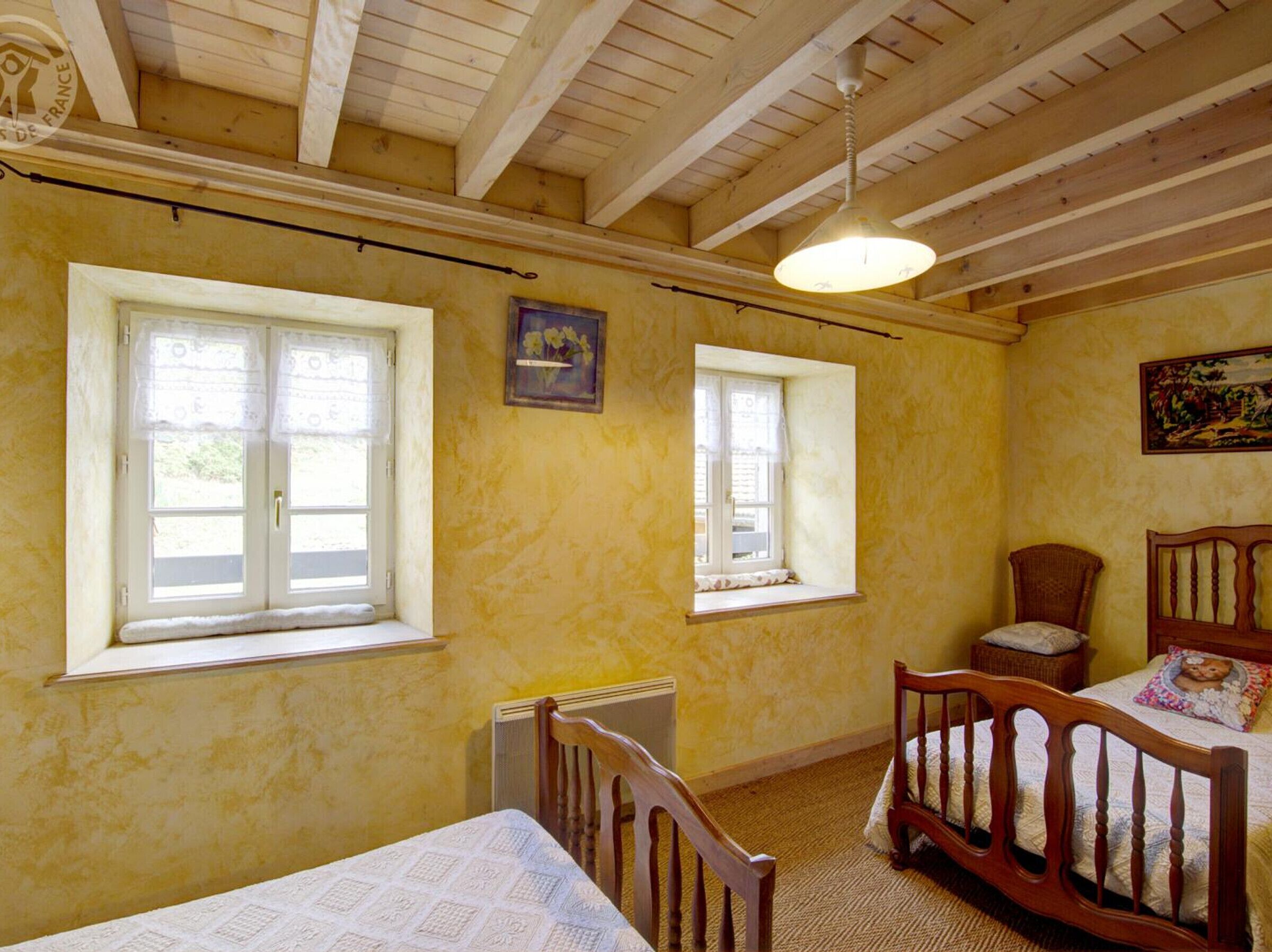 Een kamer met twee ramen, een radiator, een bed, een stoel en een plafondventilator.