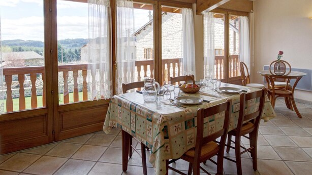 Een eethoek met een tafel voor vier personen, houten stoelen en uitzicht op het buitengebied door grote ramen.