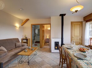 A cozy living room with a sofa, a coffee table, and a fireplace. There is a dining area with a table set for two.