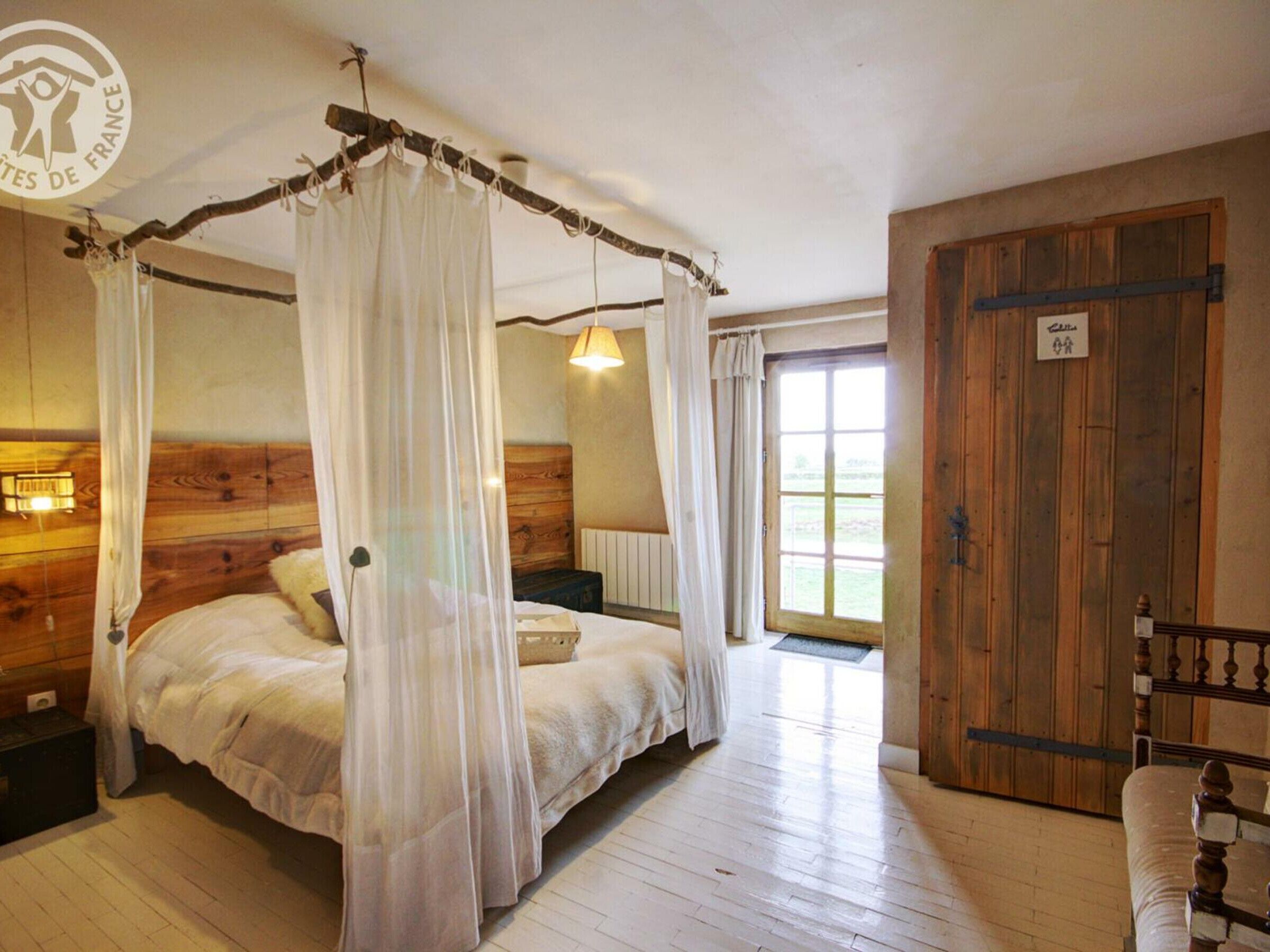 Een kamer met een hemelbed, houten wanden, een houten deur en een raam met gordijnen.