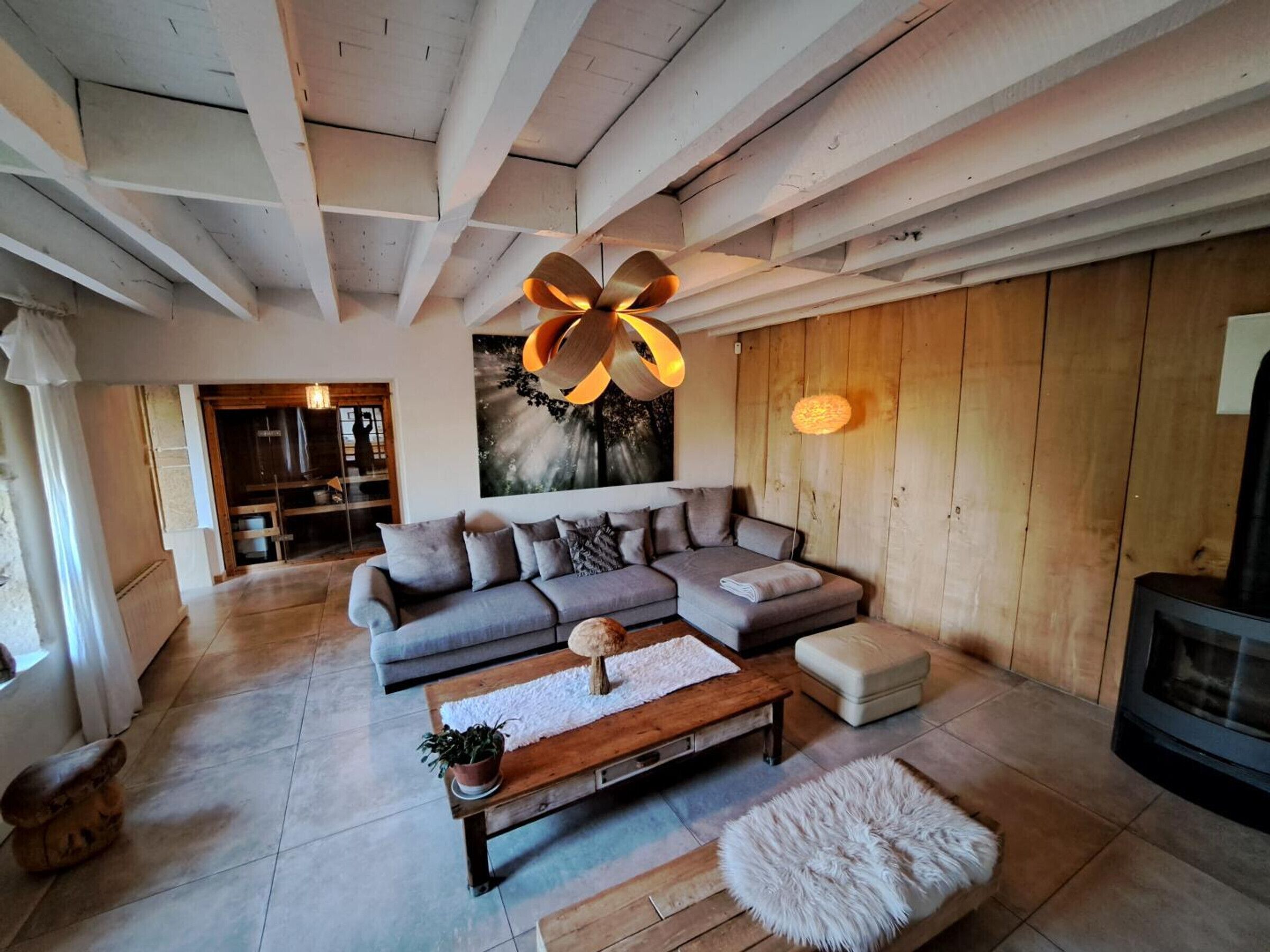 A modern living room with a sectional sofa, a wooden coffee table, and a fluffy ottoman. A large abstract painting hangs on the wall, and there is a fireplace on the right.