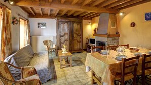 Un salon chaleureux avec un plafond en bois, une cheminée, une table à manger dressée pour quatre personnes et un canapé.