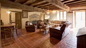 A rustic interior with exposed wooden beams, a stone wall mural, leather furniture, and a tiled floor. - Authentic cottage for 12 with terrace in countryside (Saint-Just-la-Pendue)