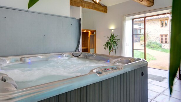A hot tub with controls, a wooden ceiling beam, and a view of a stone building outside. - Authentic cottage for 12 with terrace in countryside (Saint-Just-la-Pendue)