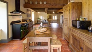 A rustic kitchen with a wooden table, a stove, and a hanging light fixture. - Authentic cottage for 12 with terrace in countryside (Saint-Just-la-Pendue)