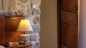 Una mesita de noche de madera con una lámpara, un muro de piedra y una puerta de madera.