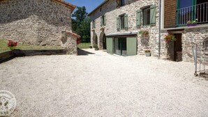 Un edificio de piedra con un patio de grava, que cuenta con una puerta central y ventanas con contraventanas.