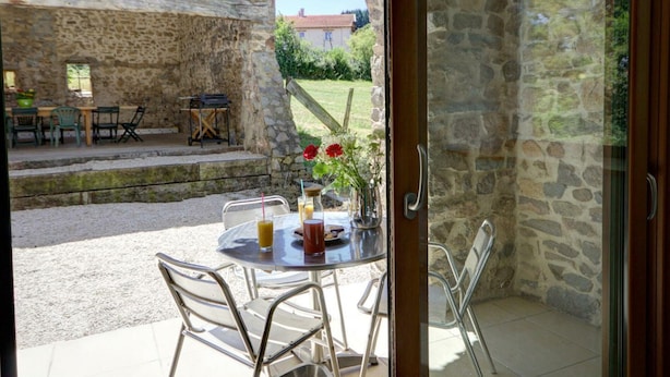 Un patio de piedra con una mesa y sillas, un muro de piedra y vistas a un jardín.