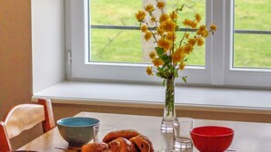 Ruokapöytä, jonka päällä on maljakko, jossa on keltaisia kukkia, lautanen täynnä leivonnaisia sekä erilaisia kulhoja ja laseja.