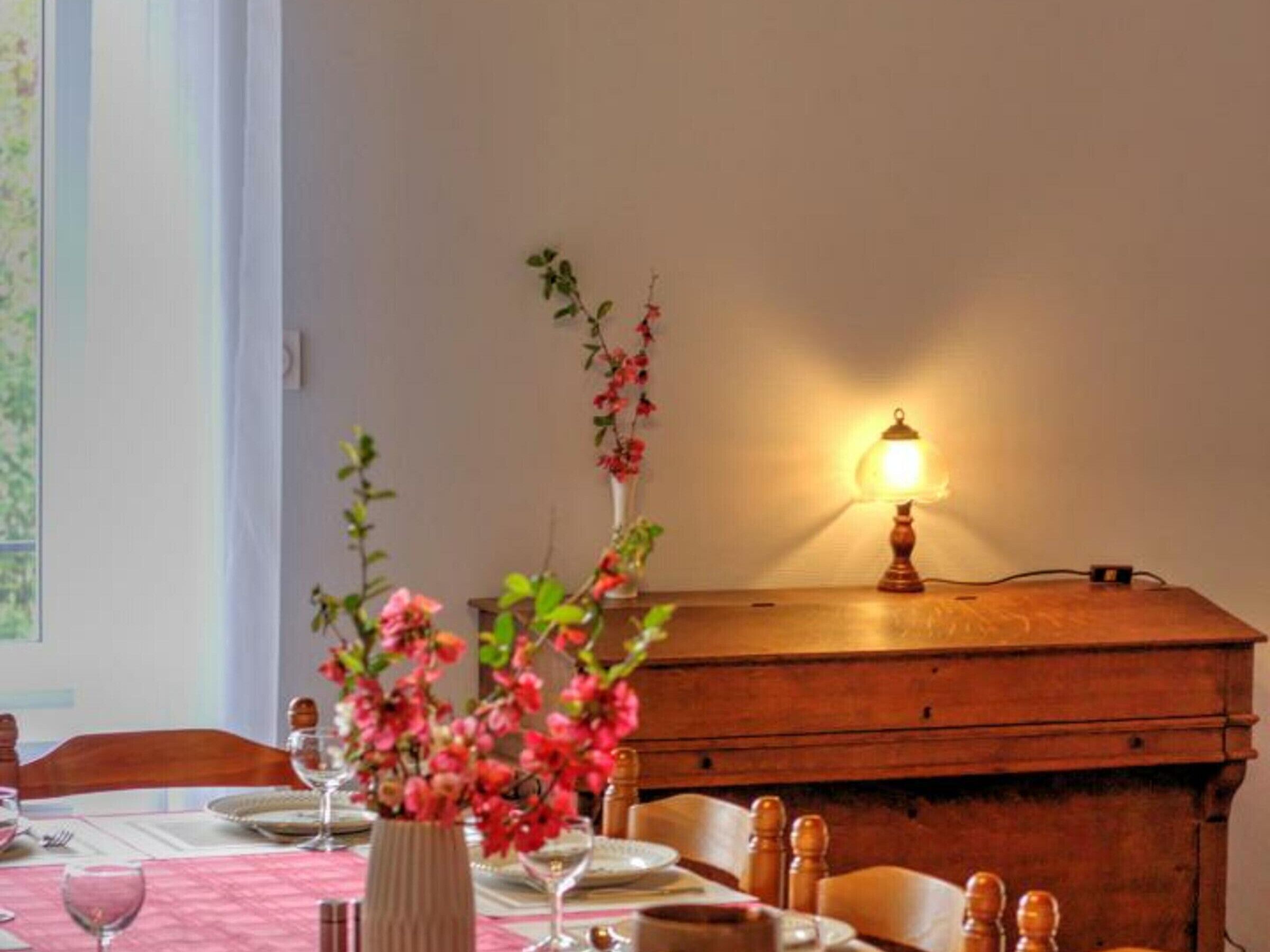 Ein Esstisch ist gedeckt mit Tellern, Gläsern und einer Blumenvase.
