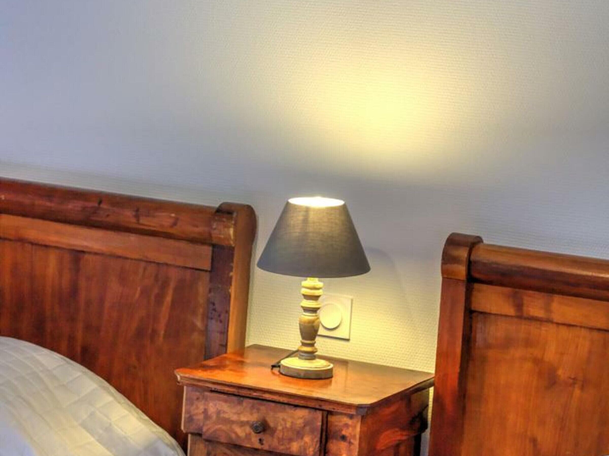 A wooden bedside table with a lamp, a drawer, and a wall socket.