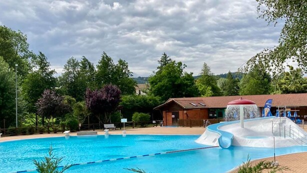 Una piscina con uno scivolo acquatico, circondata da alberi e da un edificio con tetto rosso.