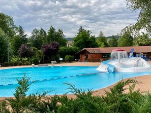 A swimming pool with a water slide, surrounded by trees and a building with a red roof. - Spacious lodging in nature with fireplace and outdoor activities (Saint-Romain-d'Urfé)