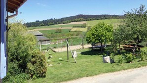 Paesaggio rurale con una casa, altalene e tavolo da picnic.