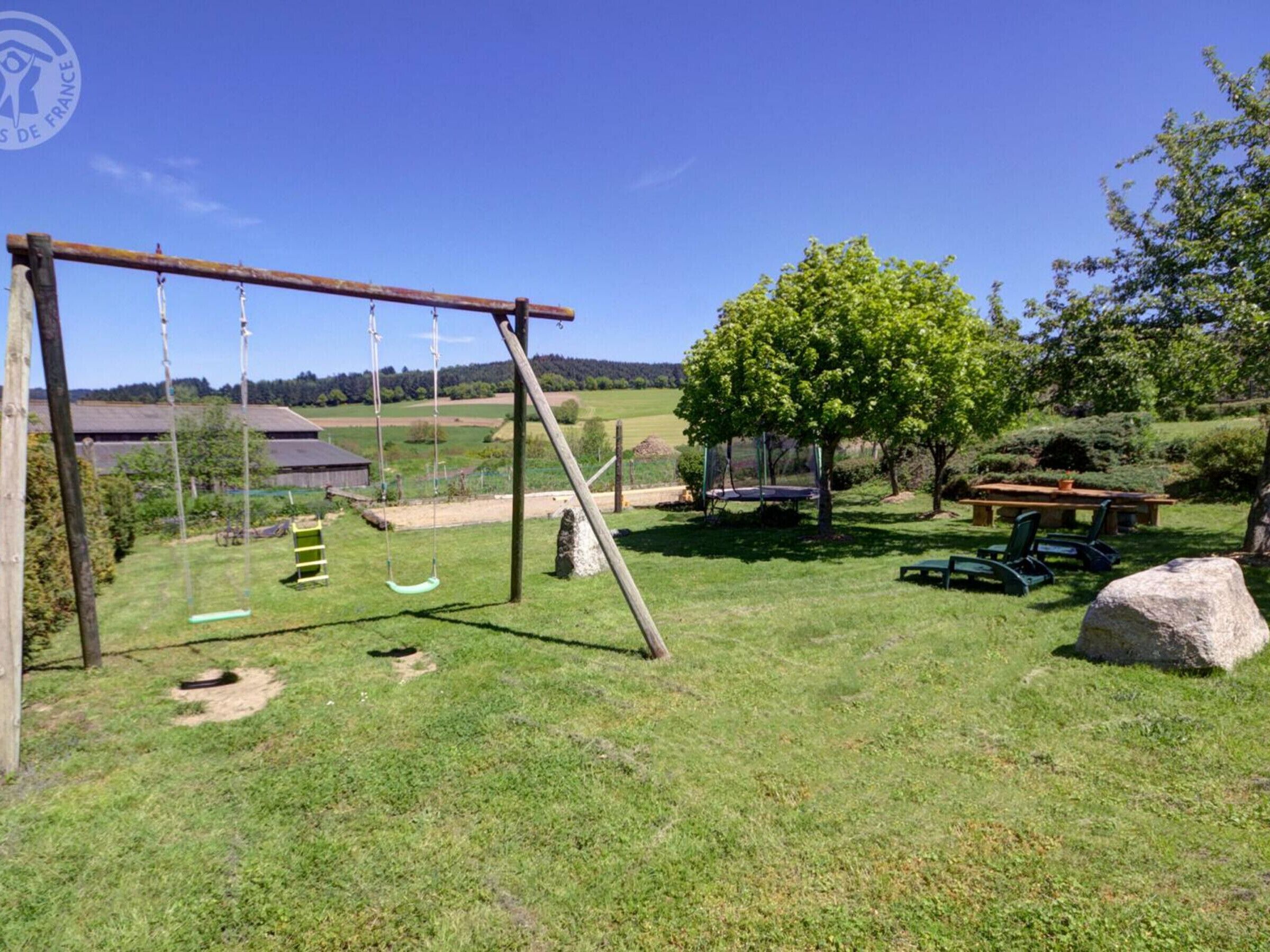 Un'area verde con altalene, tavolo da picnic e un grosso masso.