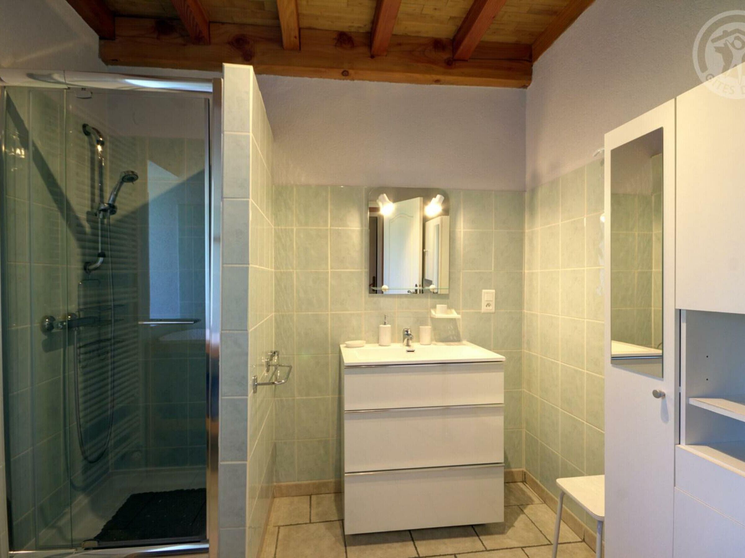 A bathroom with a glass shower enclosure, a white sink with a mirror above, and a tiled floor.