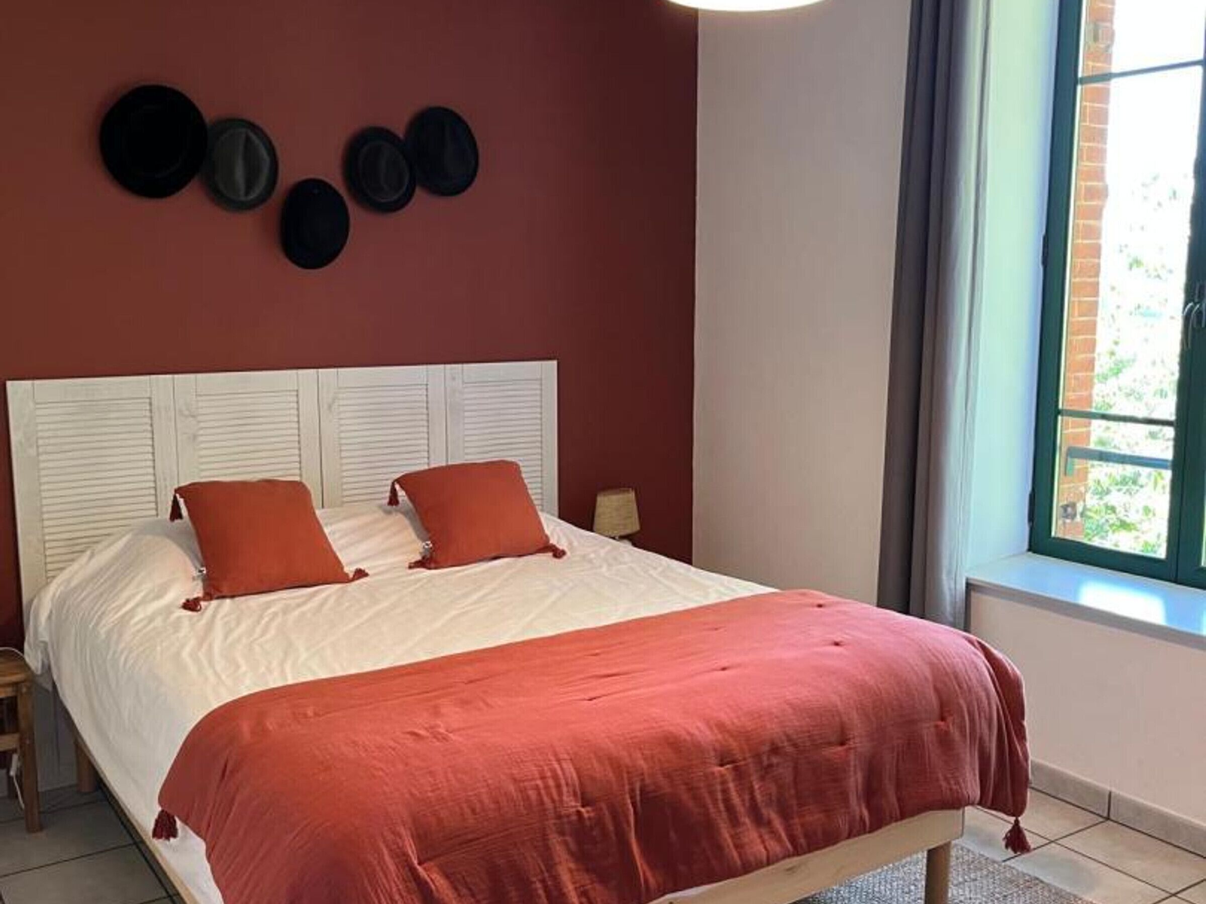 Een bed met een wit hoofdbord, twee rode kussens en een rode dekbedovertrek in een kamer met een rode muur en een raam.