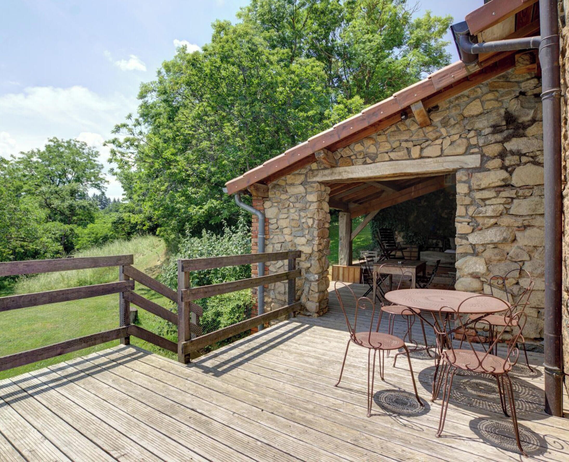 A stone building with a wooden deck, outdoor seating, and a view of a green landscape.