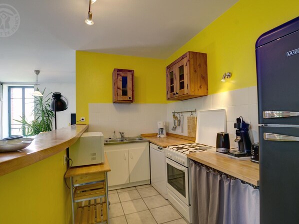 A kitchen with yellow walls, wooden cabinets, a gas stove, a refrigerator, and a sink.