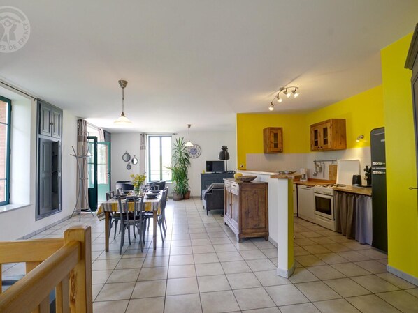 Une cuisine moderne aux murs jaunes, un coin repas avec une grande table et un four visible.