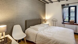 Ett sovrum med en säng, en stol, en lampa, ett fönster med utsikt och ett tak med synliga takbjälkar.