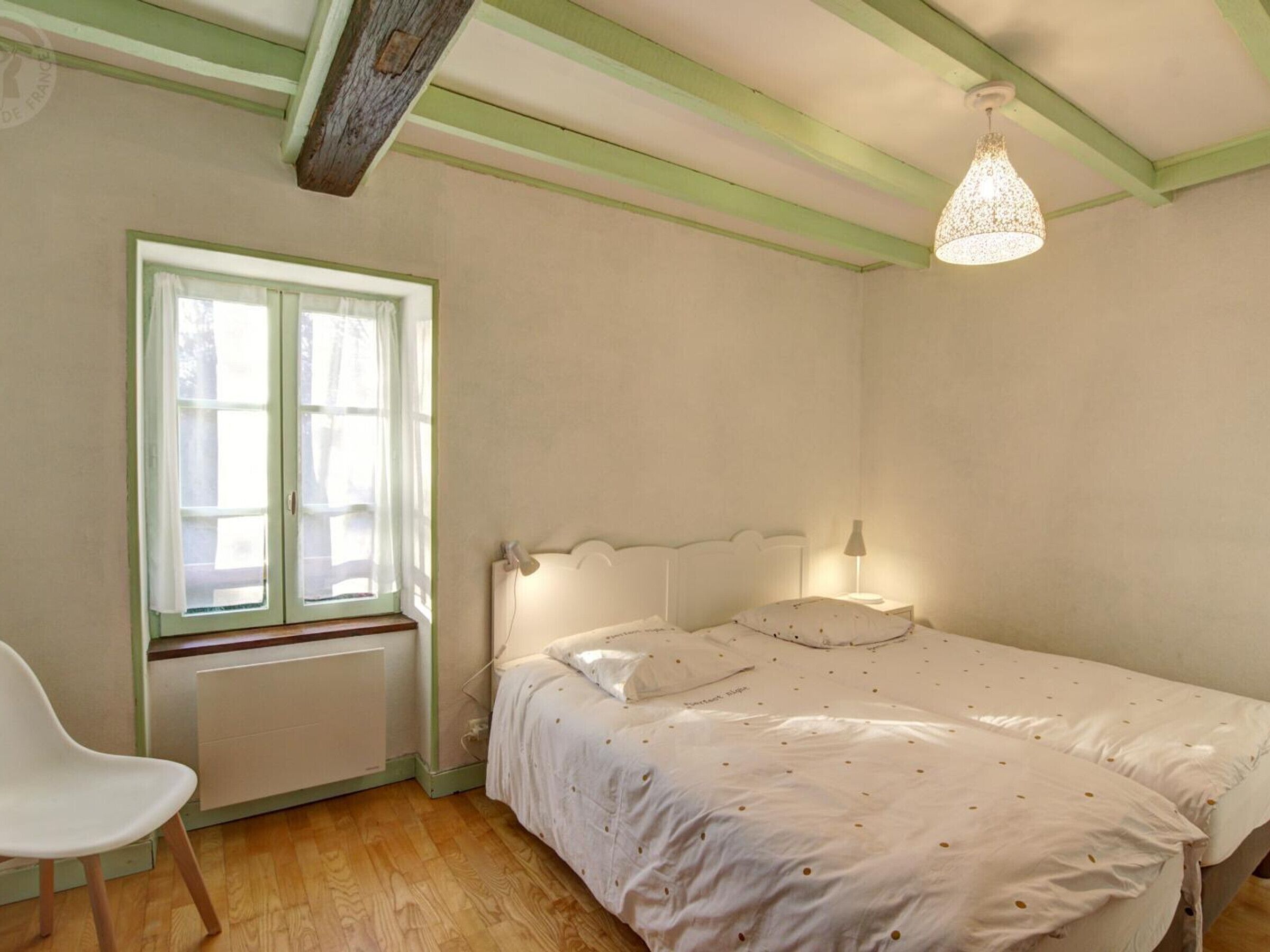 Une chambre avec un lit simple, une chaise, une fenêtre avec des rideaux et un luminaire suspendu.