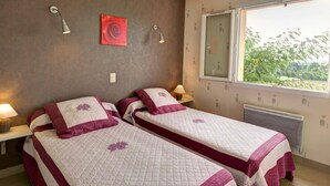 A bedroom with two beds, a window with a view, and a red rose painting on the wall. - Cottage in Saint-Forgeux-Lespinasse with Terrace and Pets Allowed (Saint-Forgeux-Lespinasse)