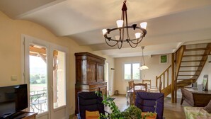 A spacious living room with a television, a dining area, and a staircase. - Cottage in Saint-Forgeux-Lespinasse with Terrace and Pets Allowed (Saint-Forgeux-Lespinasse)