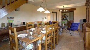 A dining area with a wooden table set for four, surrounded by chairs. A kitchen is visible in the background. - Cottage in Saint-Forgeux-Lespinasse with Terrace and Pets Allowed (Saint-Forgeux-Lespinasse)