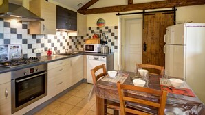A compact kitchen with a gas stove, microwave, and oven. There is a dining table with chairs and a wooden door in the background. - Cottage in Saint-Forgeux-Lespinasse with Terrace and Pets Allowed (Saint-Forgeux-Lespinasse)
