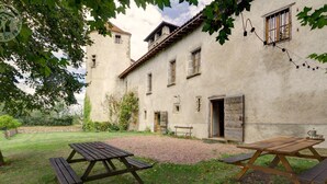 A rustic building with a stone facade, a wooden bench, and picnic tables in a grassy courtyard.