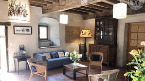 A rustic room with exposed wooden beams, a blue sofa, wicker chairs, a coffee table, and a bookshelf.