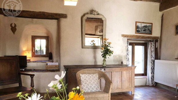 A rustic room with a wooden bench, a wicker chair, a vase with flowers, a mirror, and a framed picture on the wall.