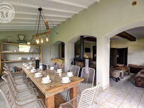 Comedor con una larga mesa de madera dispuesta para una comida, rodeado de sillas de mimbre.