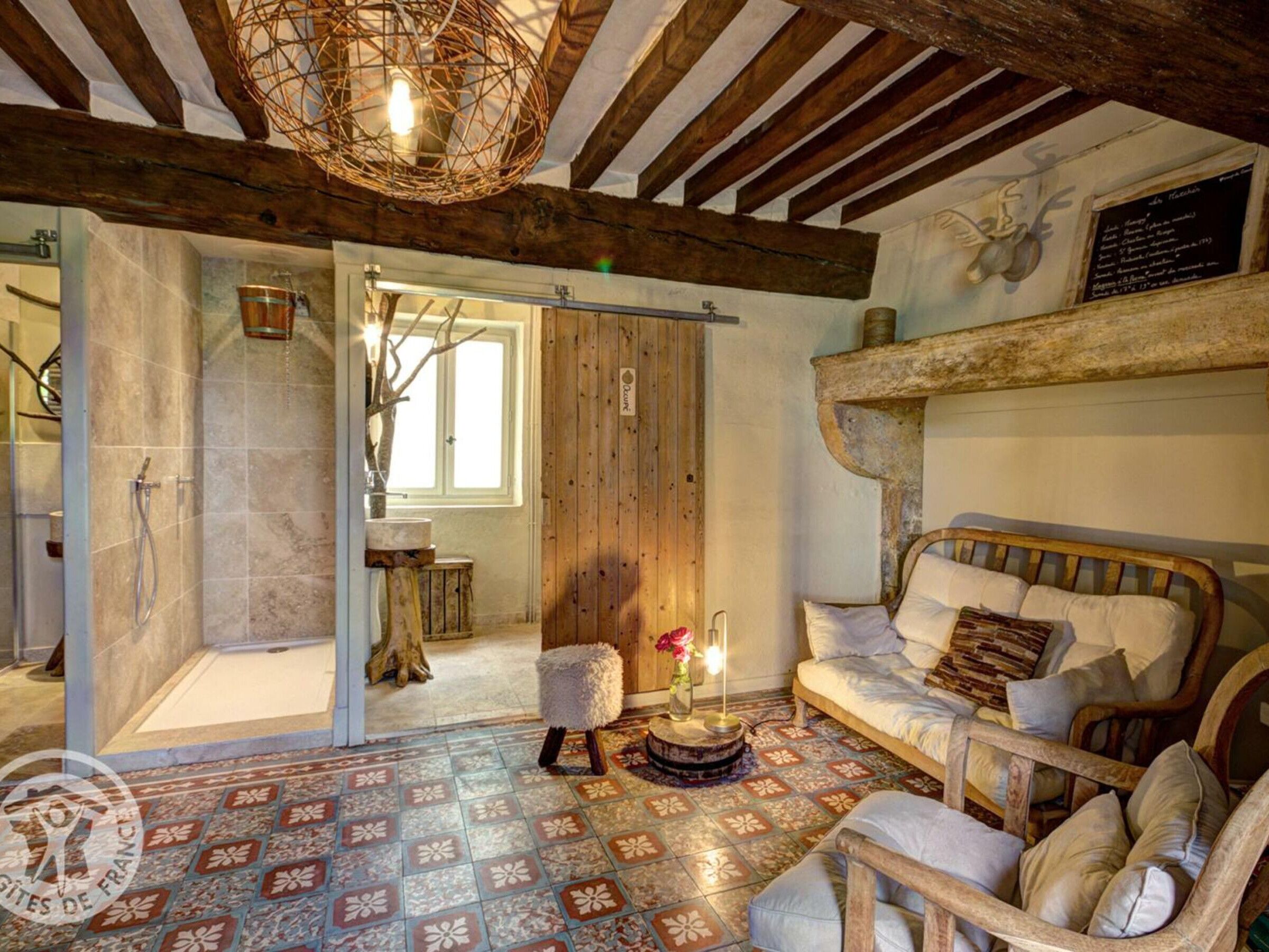 Ein rustikaler Raum mit Holzbalkendecke, einem Bett mit vielen Kissen, einem kleinen Tisch mit einer Vase und einem gemusterten Boden.