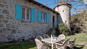 A stone building with a tower, outdoor seating with chairs and a table, and a clear sky.