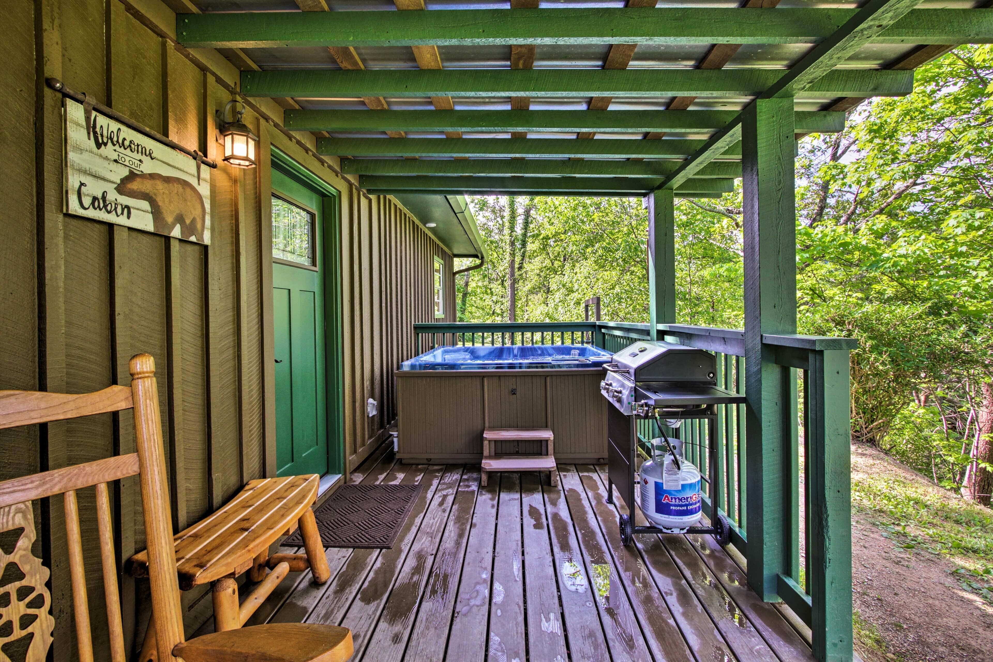 A wooden deck with a hot tub, a bench, and a sign welcoming visitors to the cabin.