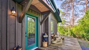 Une cabane en bois avec une porte verte, une terrasse en bois et deux sculptures d’ours.