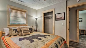 Une chambre avec un grand lit, une fenêtre avec des stores, une lampe sur pied, un porte-manteau et une porte donnant sur une autre pièce.