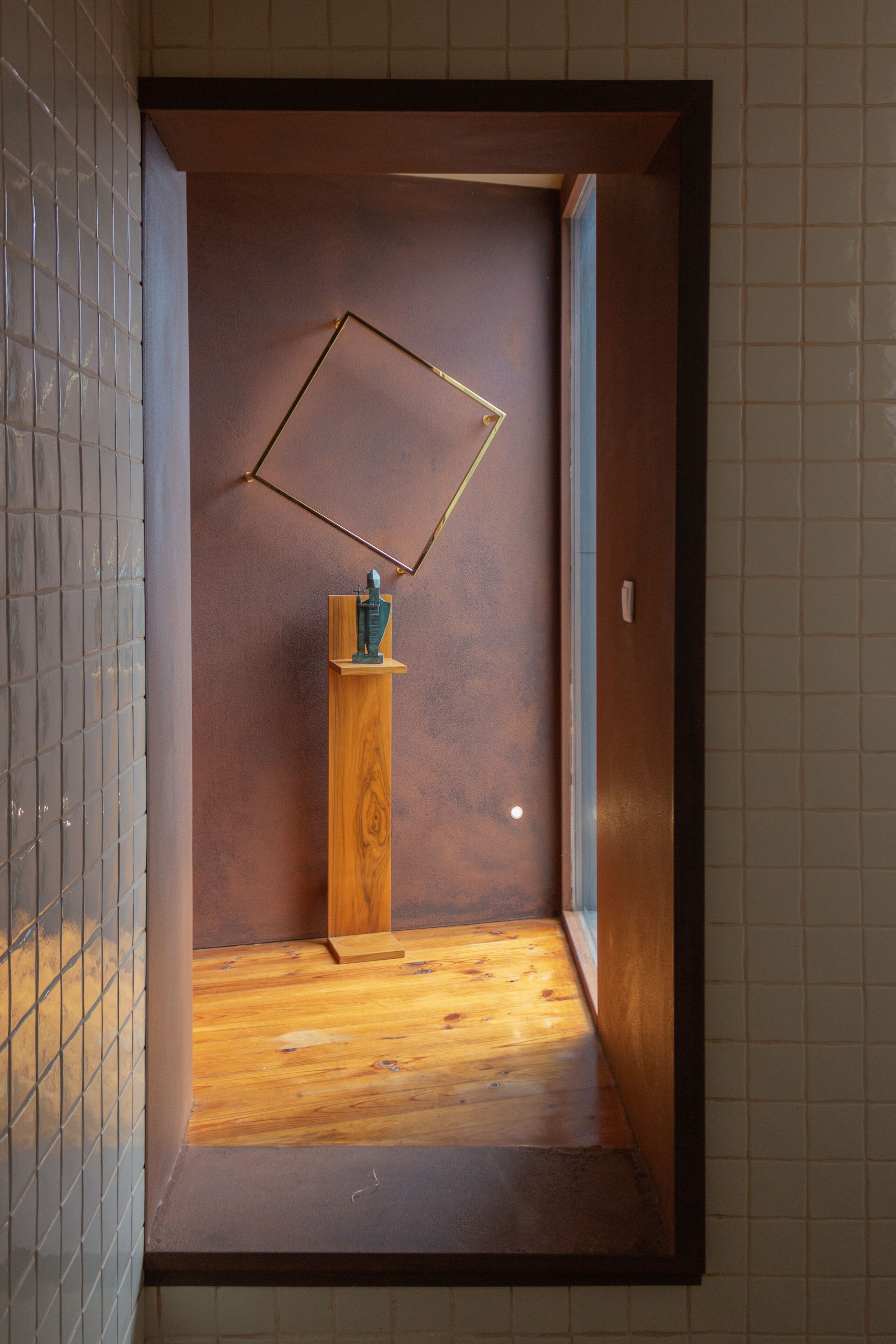 A narrow hallway with a wooden floor, a wooden pedestal with a sculpture, and a geometric wall decoration.