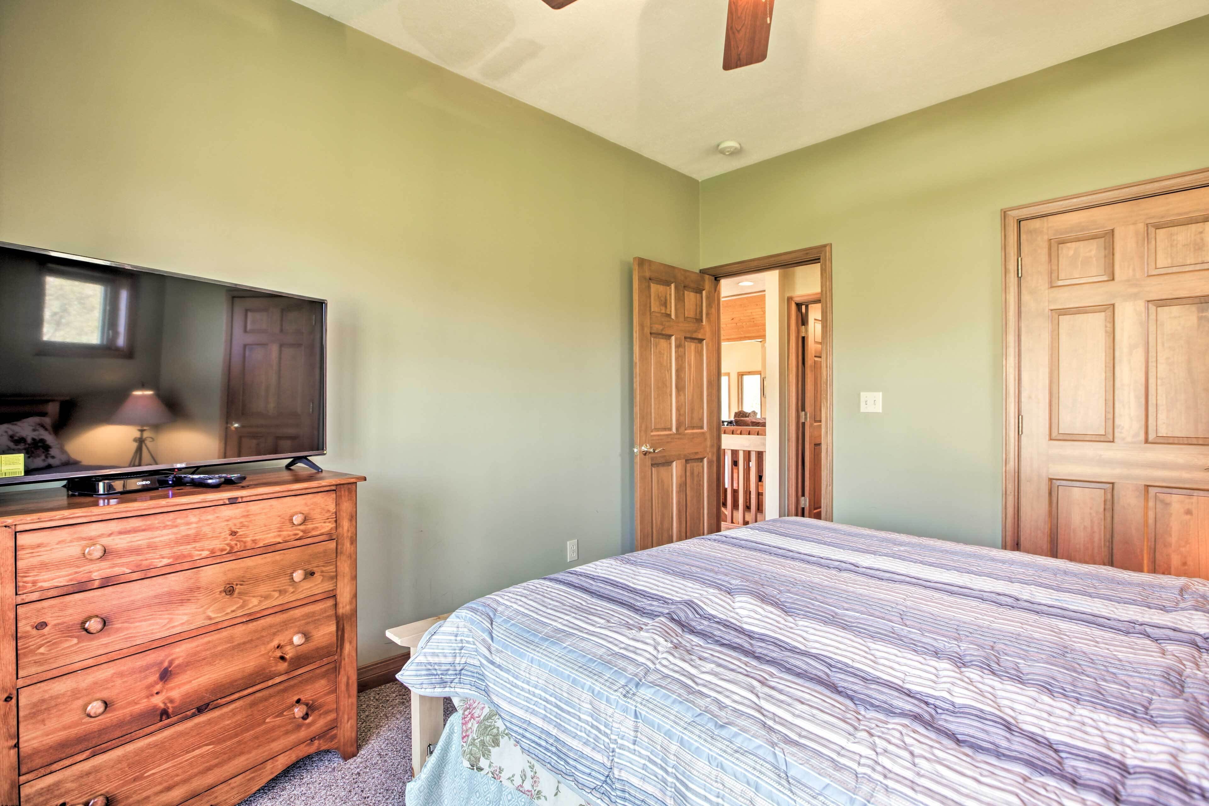 A bedroom with a bed, dresser, television, and a door leading to another room.