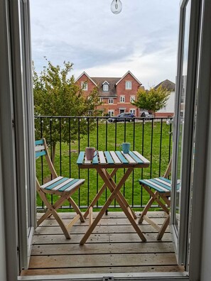 Un balcone con tavolo e sedie, vista su un edificio residenziale e cielo sereno.