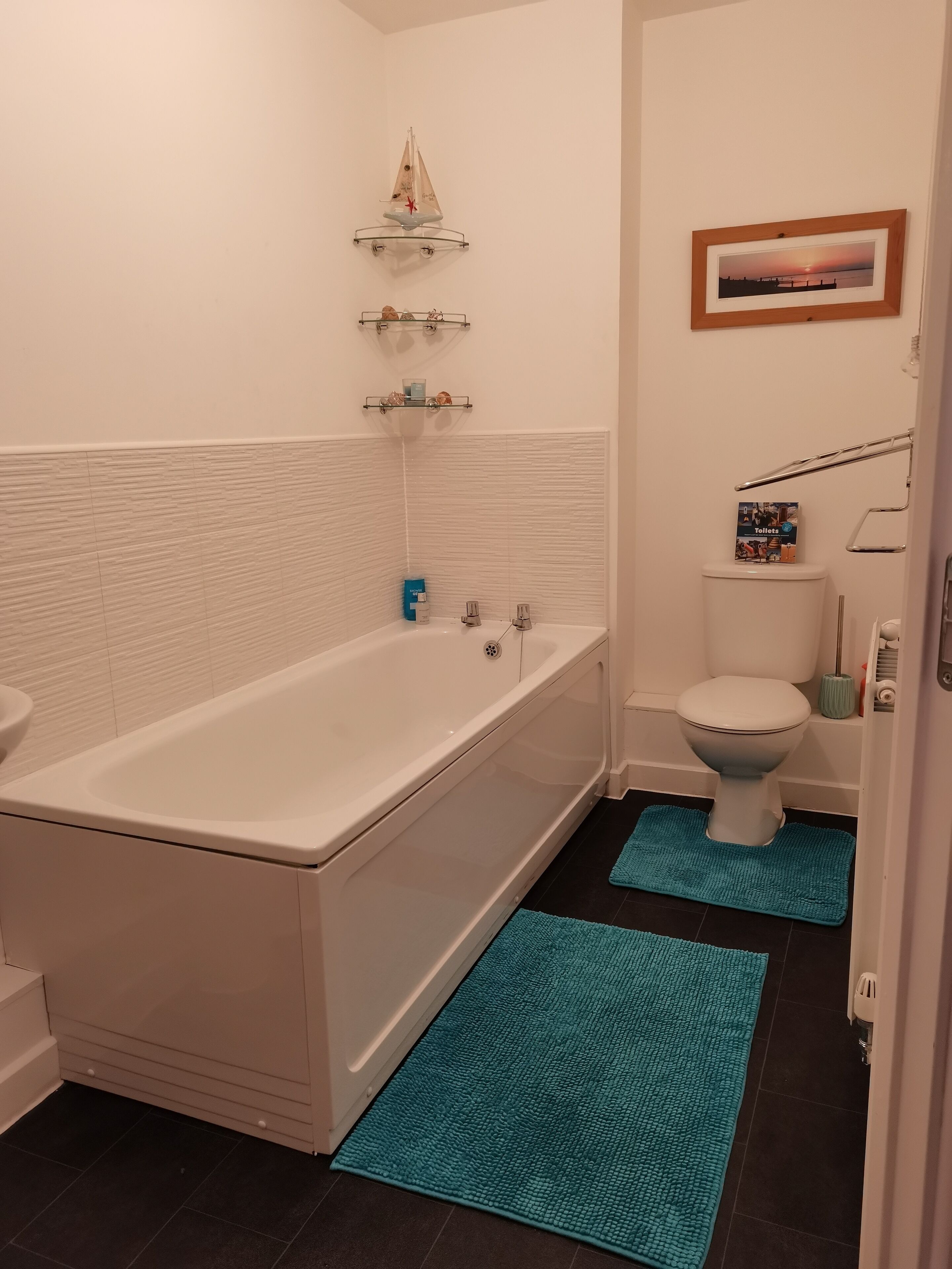 Een badkamer met een bad, toilet en een plankje met een klein model zeilboot.