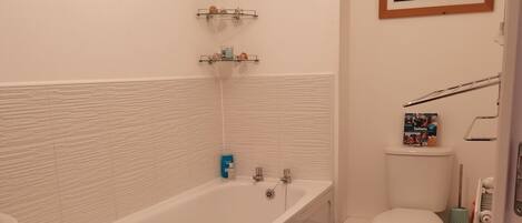 Een badkamer met een bad, toilet en een plankje met een klein model zeilboot.