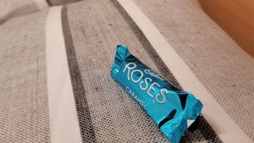 A bed with a striped blanket and a blue candy wrapper labeled "ROSES CARAMEL" on it.